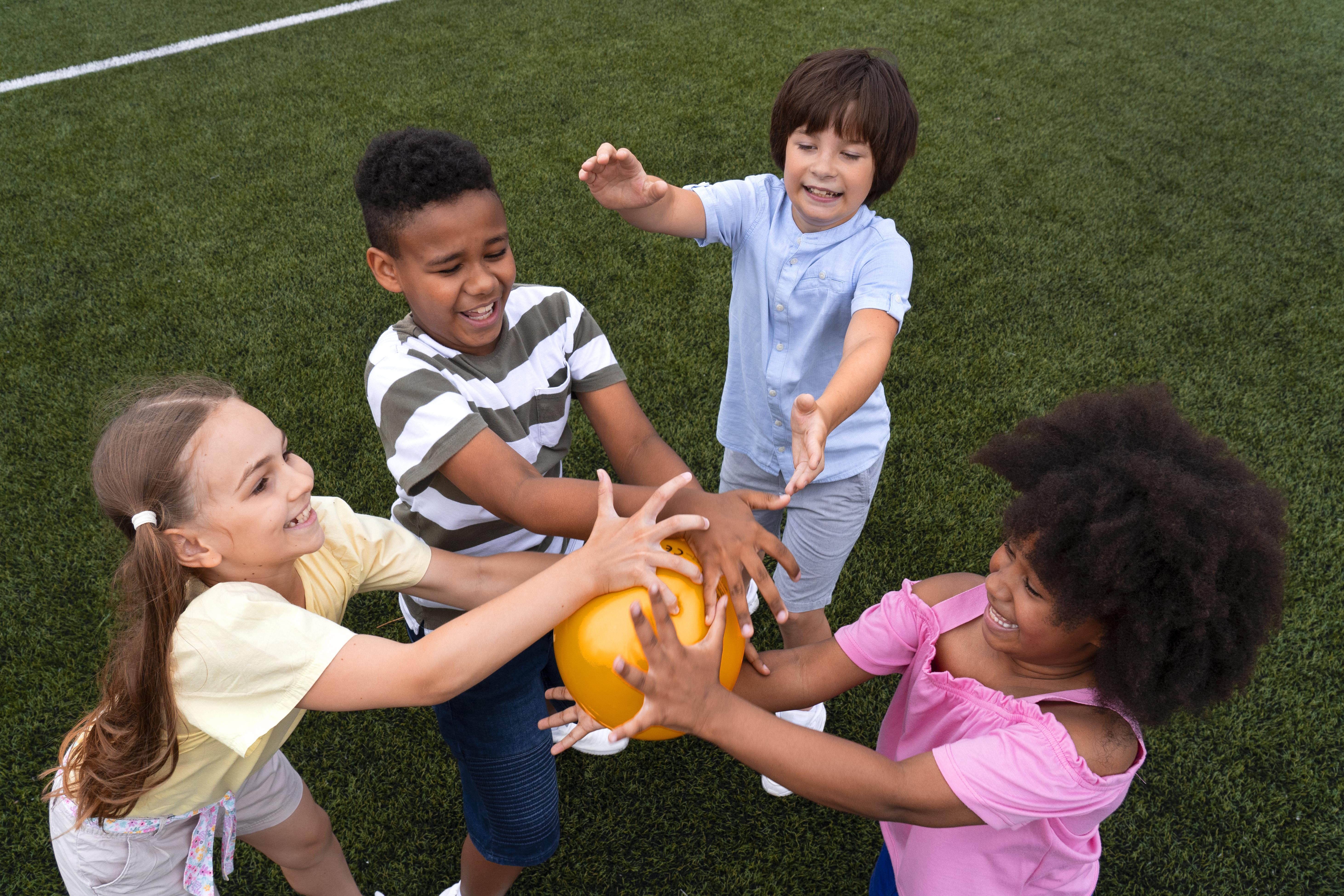 A diverse group of smiling children playing together with a ball outdoors, representing the young people the foundation supports